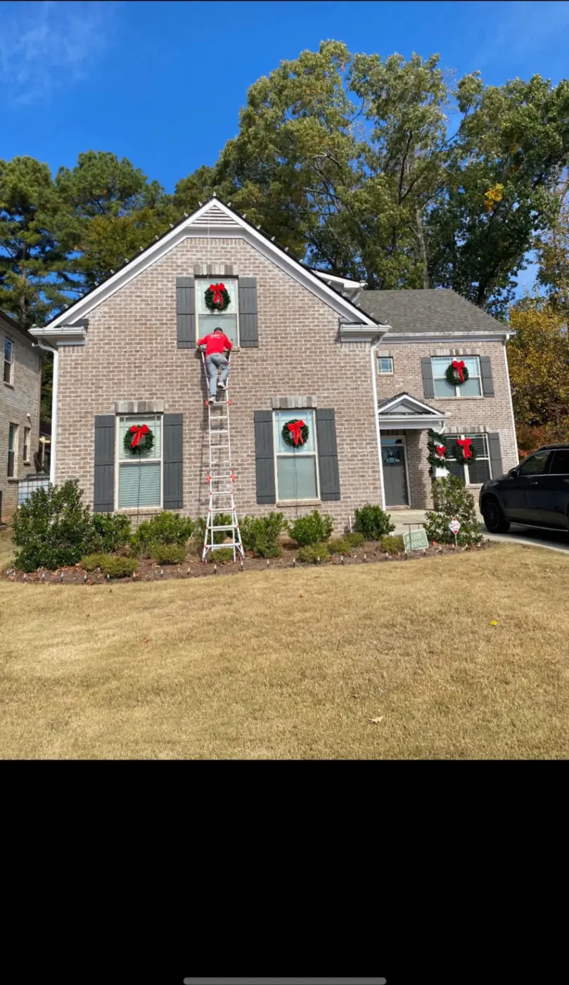 Professional installer placing holiday wreaths on a residential home